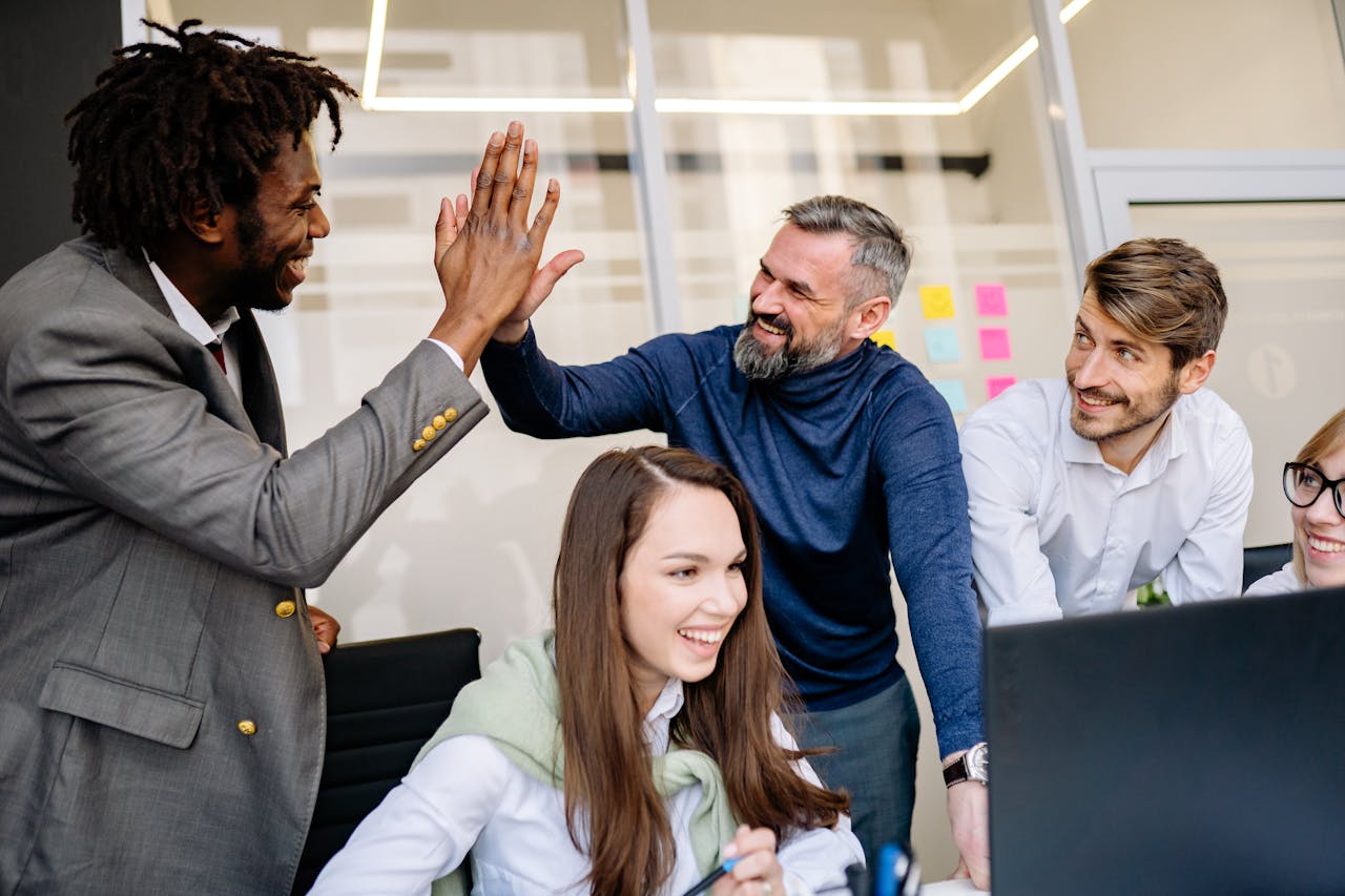 A diverse team happily celebrates a workplace achievement with high-fives.